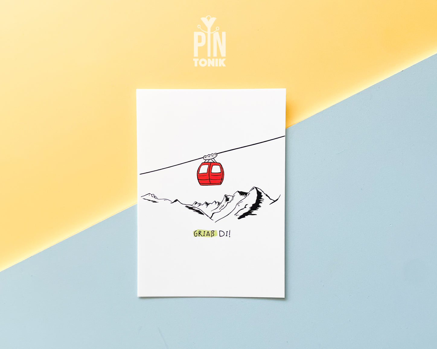 Premium postcard with an original illustration of a red cable car and the text 'Griaß Di!', shown against a vibrant yellow and blue background.