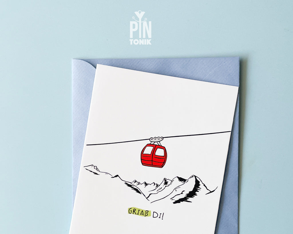 Premium postcard with an original illustration of a red cable car and the text 'Griaß Di!', shown against a blue background with a light blue envelope.