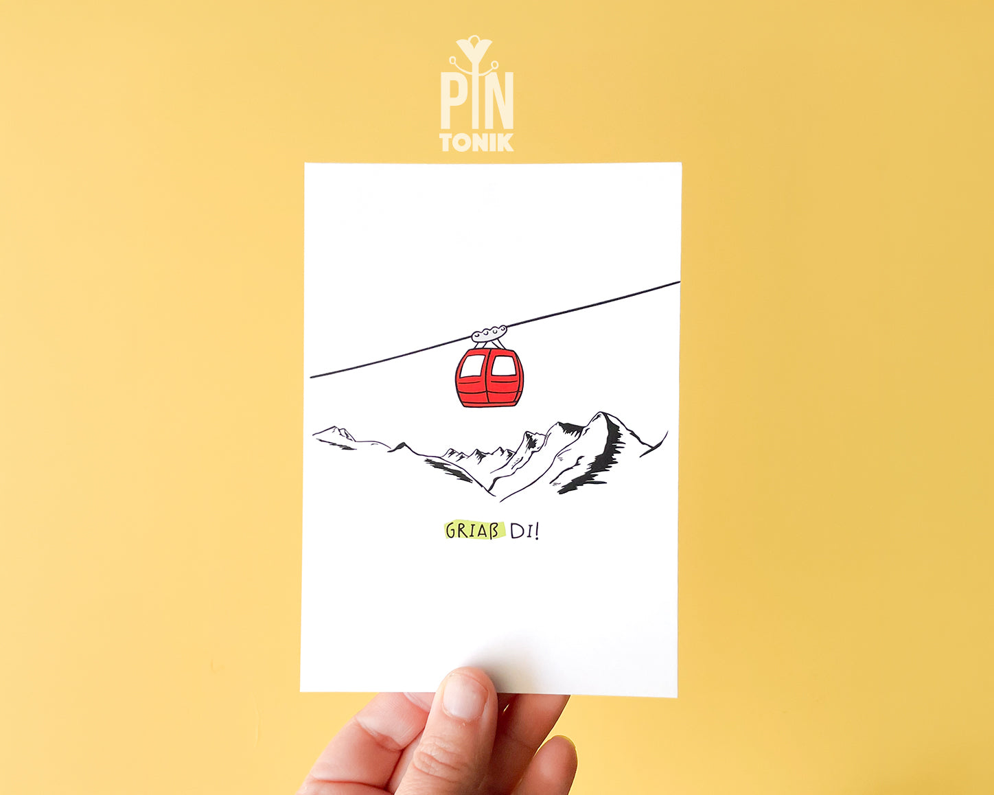 Premium postcard with an original illustration of a red cable car and the text 'Griaß Di!', shown against a vibrant yellow background with a light blue envelope.