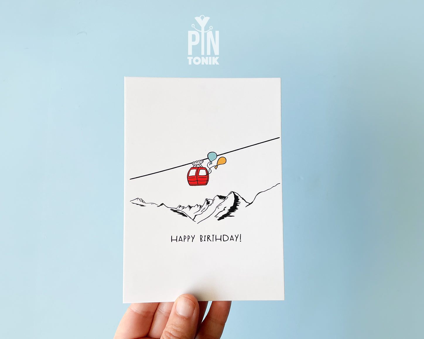 Premium postcard with an original illustration of a red cable car with colorful balloons and the text 'HAPPY BIRTHDAY!', shown against a blue background.