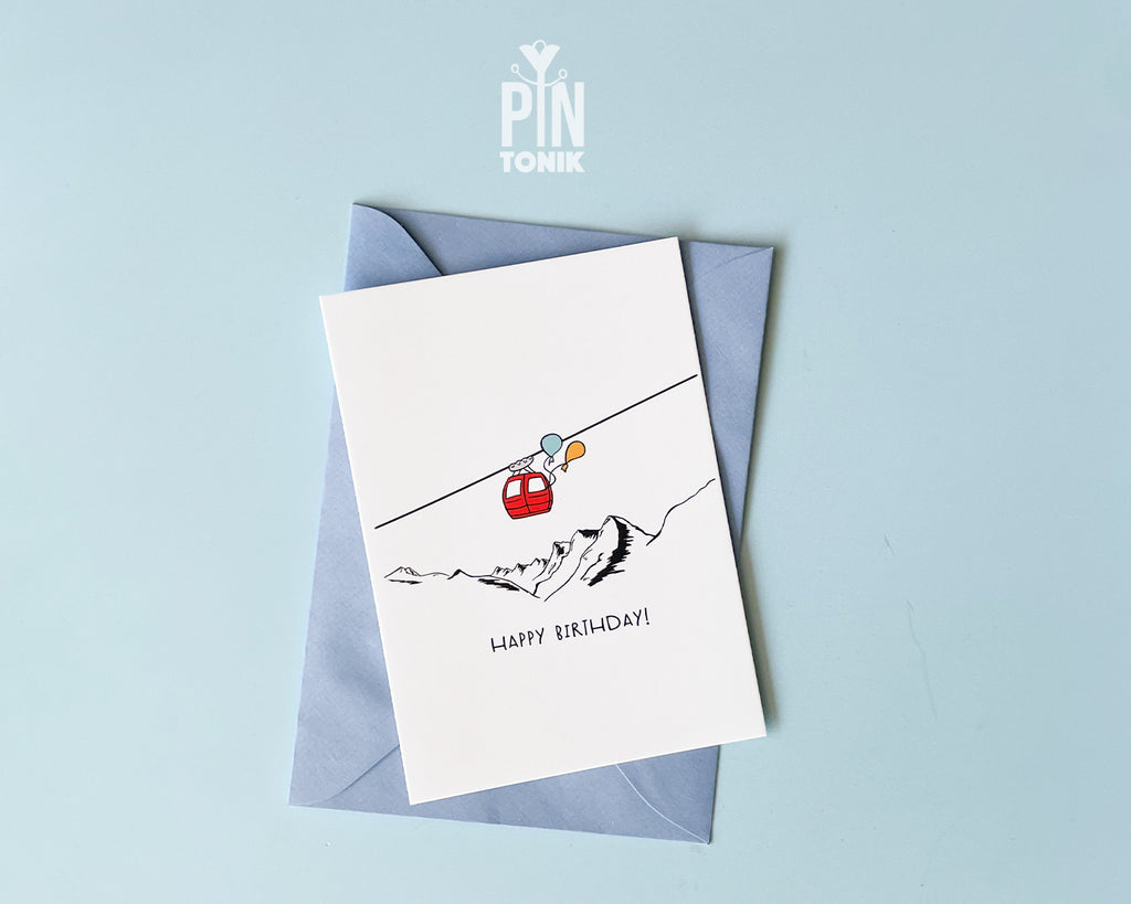 Greeting card with a red gondola and mountain illustration on a light blue background, featuring the brand 'PIN Tonik'.