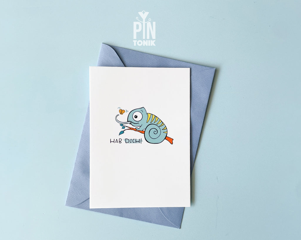 Premium postcard featuring Moji the Chameleon, the PinTonik mascot, catching a butterfly with the text 'HAB DICH!', shown with a luxury light blue envelope.