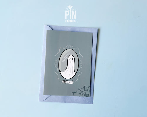 Premium grey postcard with an original illustration of a ghost in a mirror and the text 'BOO!', shown with a light blue luxury envelope on a light blue background.