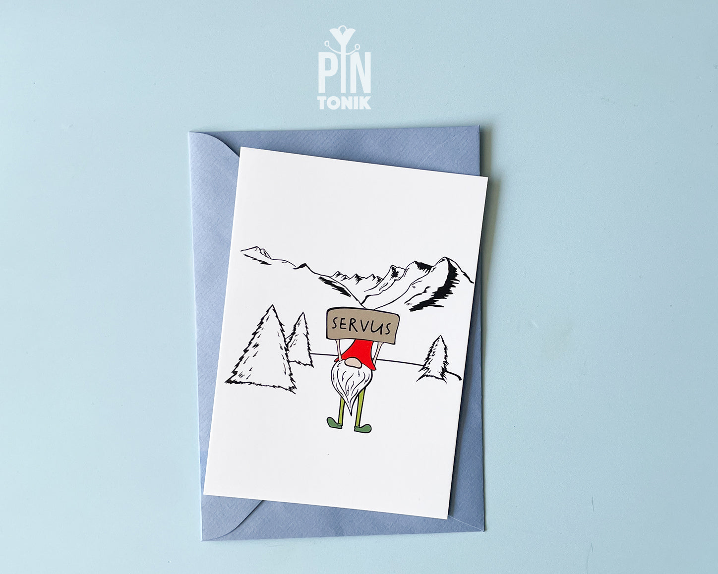 Premium postcard with an original illustration of a mountain gnome holding a 'SERVUS' sign in a snowy alpine landscape, shown with a light blue envelope.