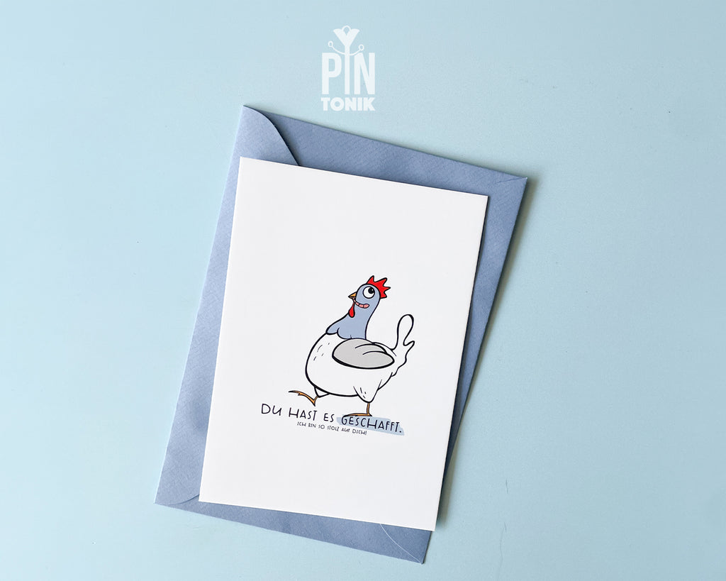 Premium postcard featuring an original hand-drawn chicken and the text 'Du hast es geschafft,' paired with a luxury blue envelope on a vibrant yellow background.