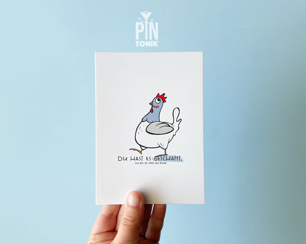 Premium postcard featuring an original hand-drawn chicken and the text 'Du hast es geschafft,' paired with a luxury blue envelope on a vibrant yellow background.