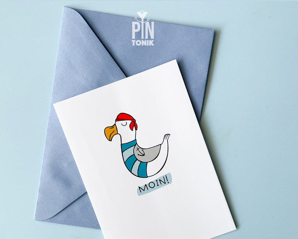 Premium postcard with an original illustration of a seagull wearing a red bandana and sailor stripes with the text 'MOIN!', shown with a light blue envelope against a soft blue background.