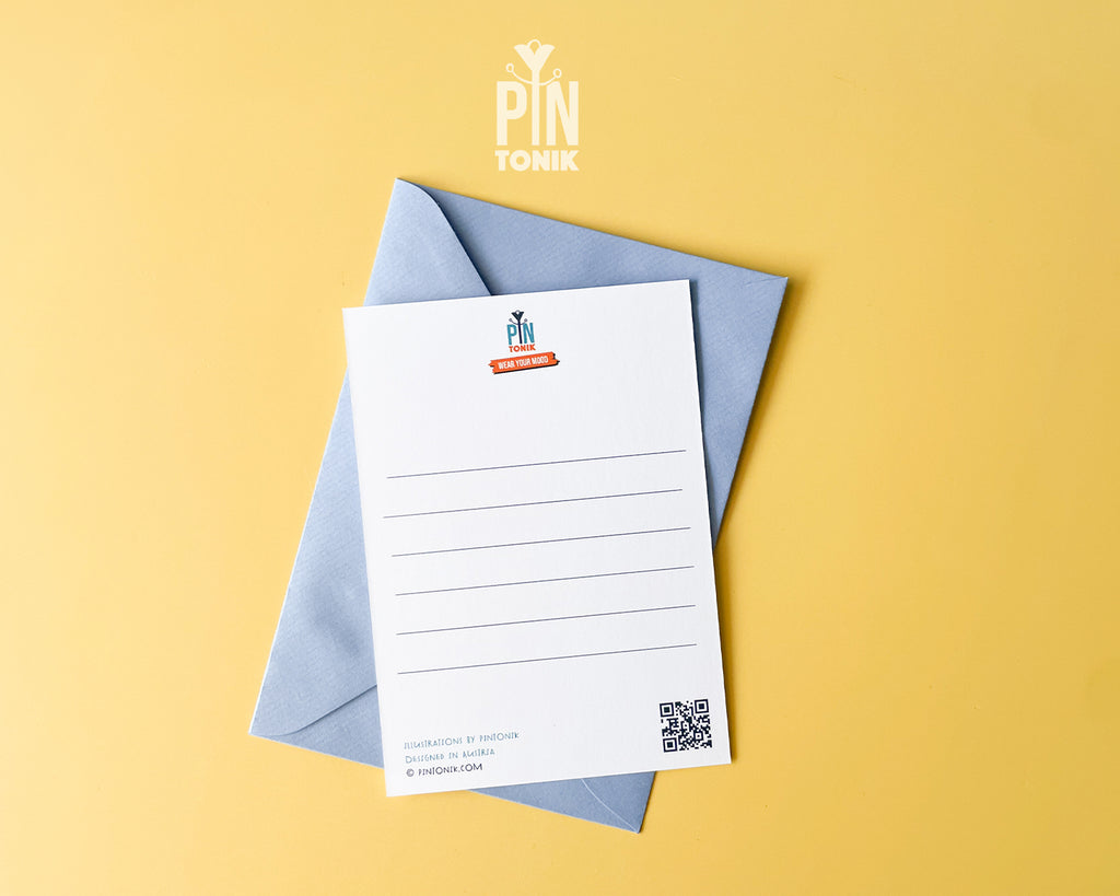 The back of a premium postcard featuring a clean, white uncoated surface with five light grey lines for a handwritten message and a QR code in the corner. An original 'PinTonik' logo with the slogan 'Wear Your Mood' is centered at the top. A luxury light blue envelope sits underneath the card against a vibrant yellow background.