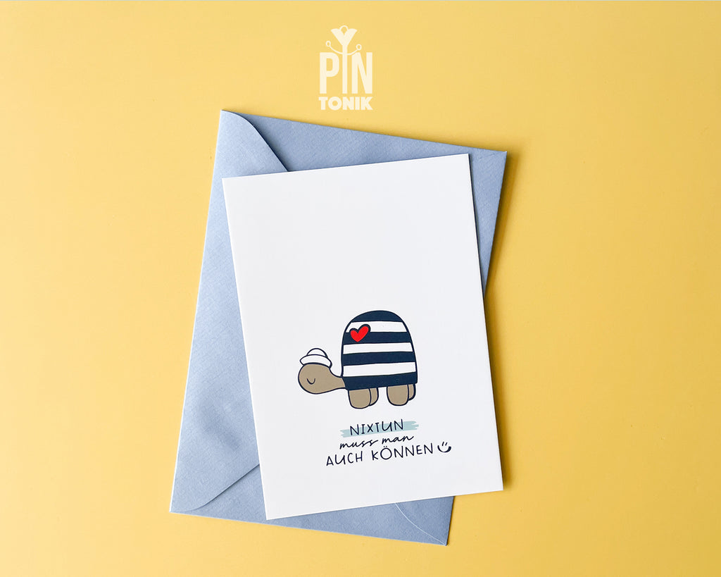 Premium postcard with an original illustration of a turtle wearing a sailor hat and striped shirt with a red heart, featuring the text 'NIXTUN muss man AUCH KÖNNEN', shown with a light blue envelope.