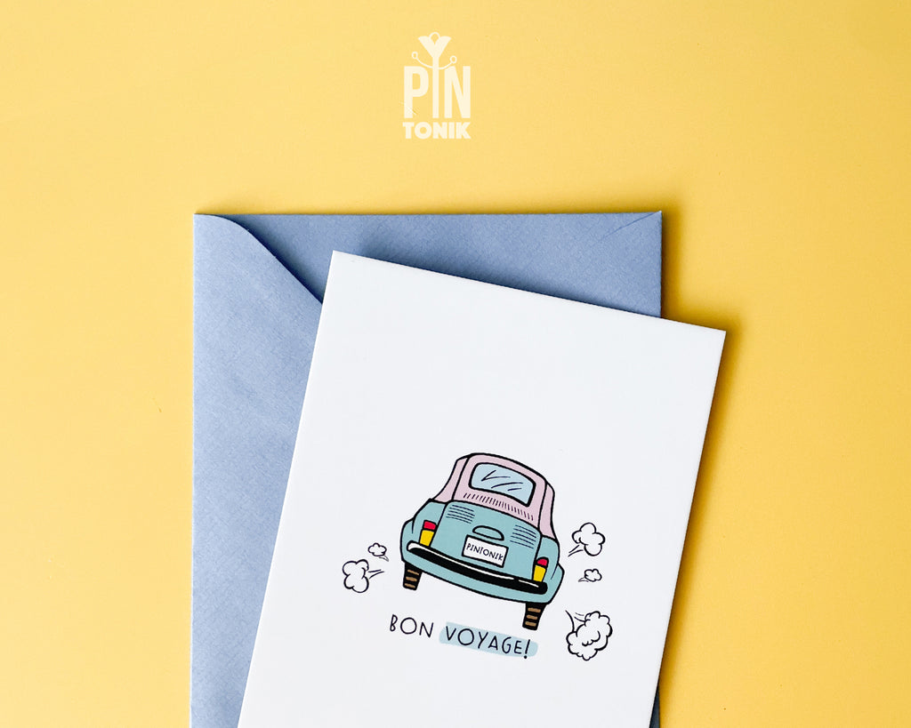 Premium postcard with an original illustration of a light blue retro car and the text 'Bon Voyage!', shown held against a light blue background.