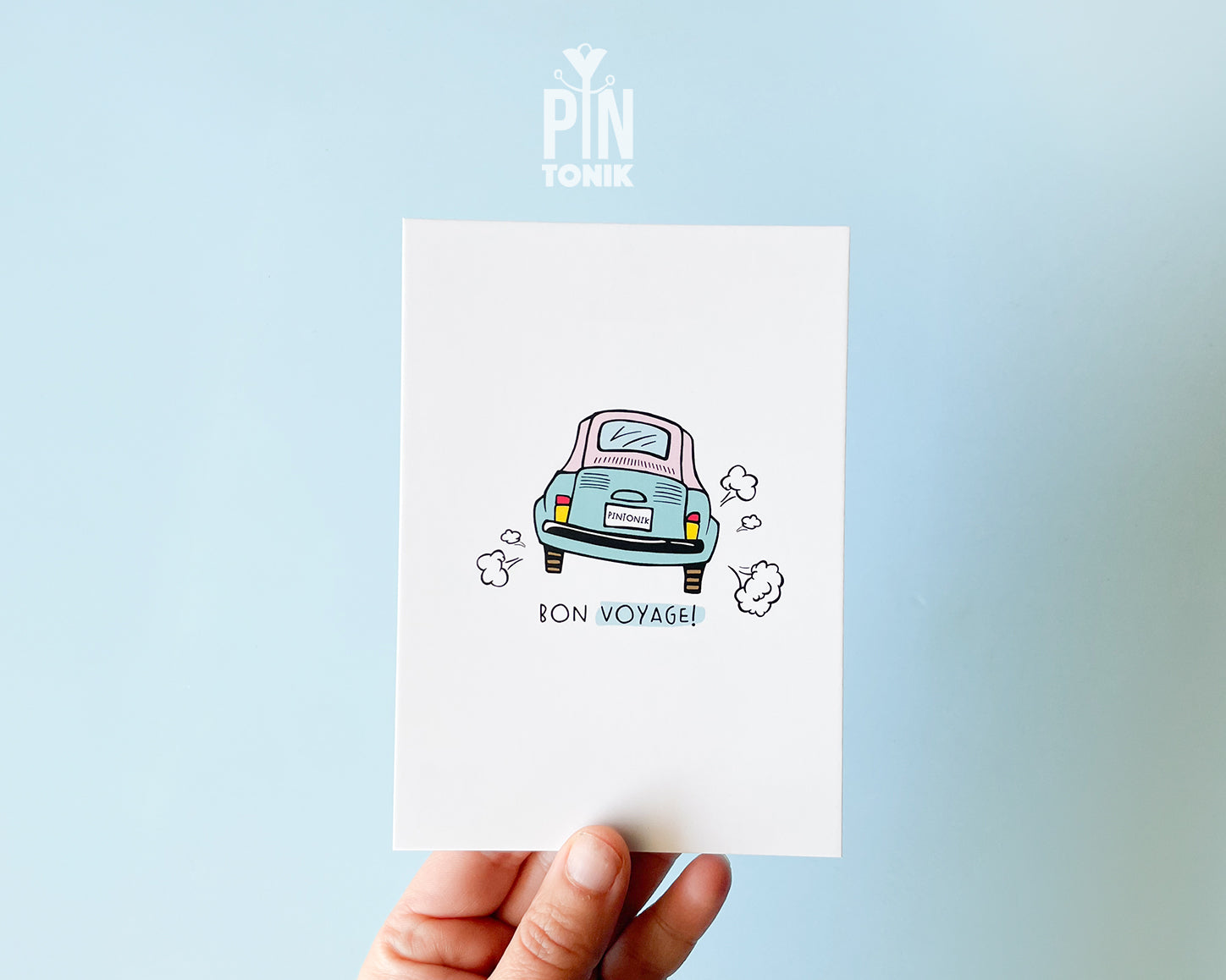 Premium postcard with an original illustration of a light blue retro car and the text 'Bon Voyage!', shown held against a light blue background.