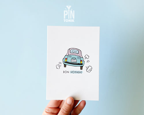 Premium postcard with an original illustration of a light blue retro car and the text 'Bon Voyage!', shown held against a light blue background.