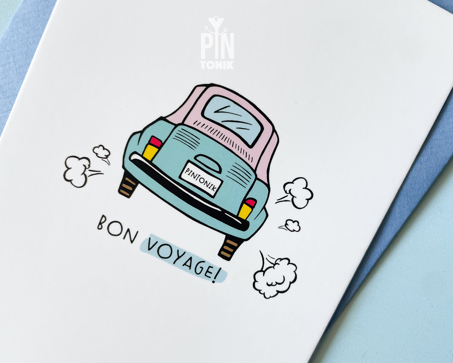 Premium postcard with an original illustration of a light blue retro car and the text 'Bon Voyage!', shown held against a light blue background.