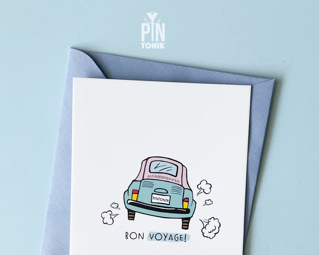 Premium postcard with an original illustration of a light blue retro car and the text 'Bon Voyage!', shown held against a light blue background.