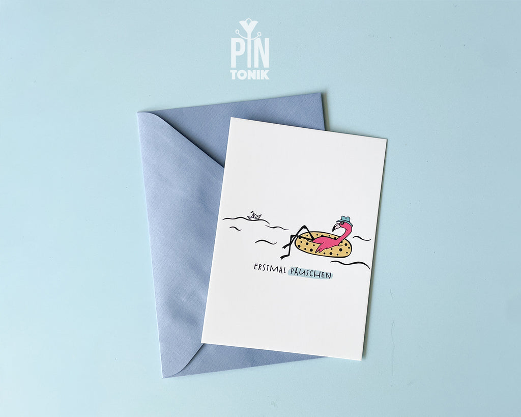 Premium postcard with an original illustration of a flamingo in a polka-dot floatie with the text 'ERSTMAL PÄUSCHEN', shown with a light blue luxury envelope on a light blue background.