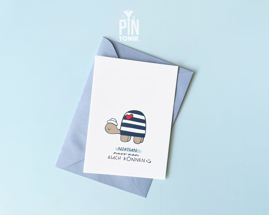 Premium postcard with an original illustration of a turtle wearing a sailor hat and striped shirt with a red heart, featuring the text 'NIXTUN muss man AUCH KÖNNEN', shown with a light blue envelope.