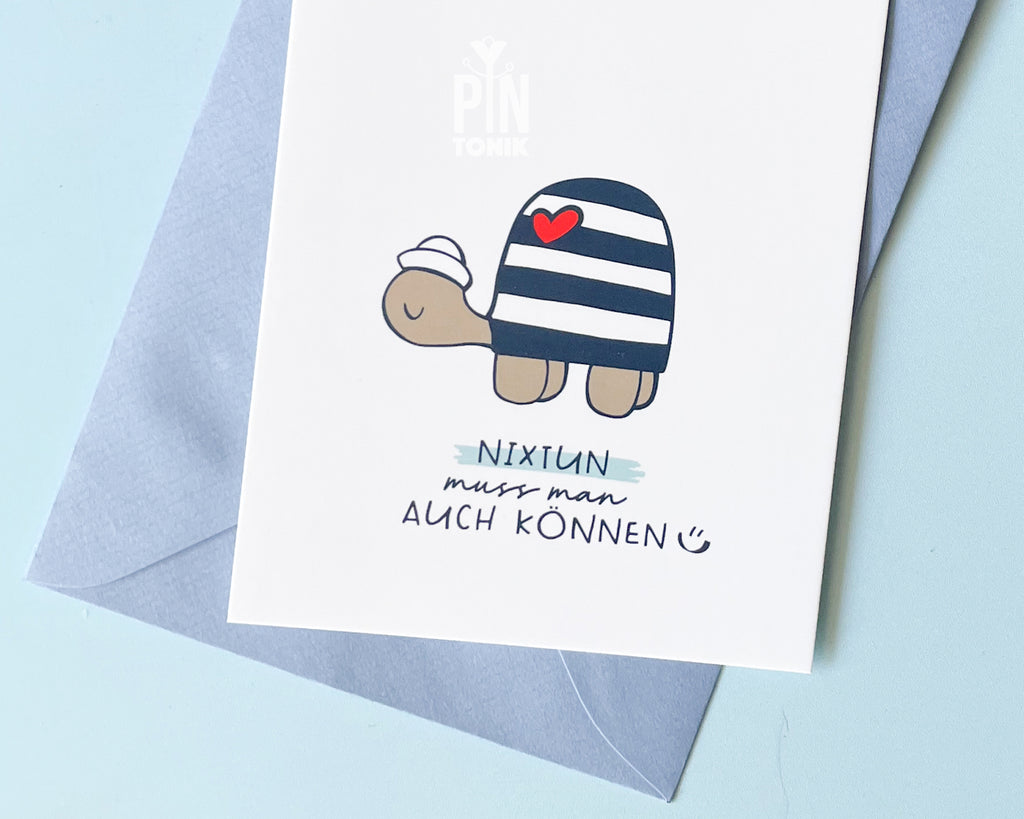 Premium postcard with an original illustration of a turtle wearing a sailor hat and striped shirt with a red heart, featuring the text 'NIXTUN muss man AUCH KÖNNEN', shown with a light blue envelope.