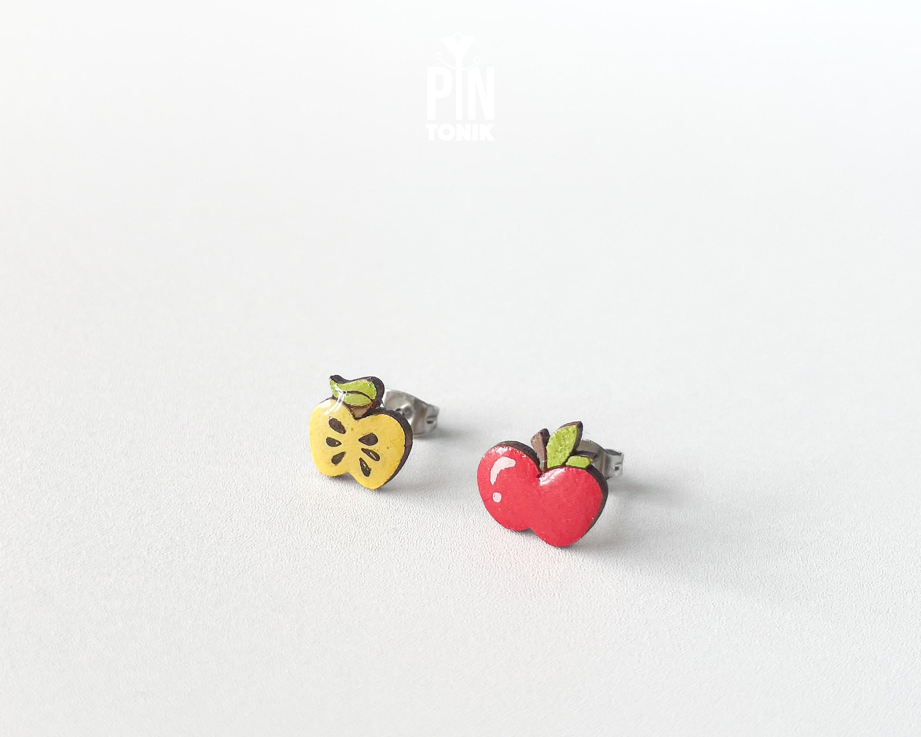 Mismatched wooden stud earrings featuring one whole red apple and one yellow apple core illustration, high-gloss epoxy finish, shown on a white background.