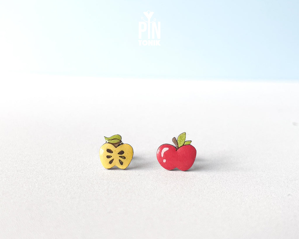 Mismatched wooden stud earrings featuring one whole red apple and one yellow apple core illustration, high-gloss epoxy finish, shown on a white background.