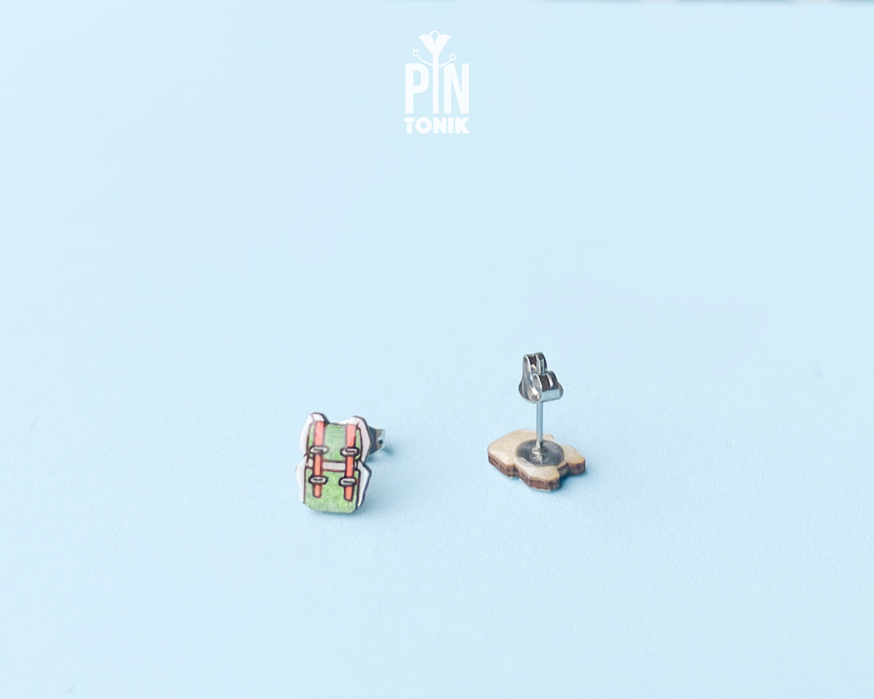 "Handmade wooden green hiking backpack stud earrings with brown strap and buckle illustrations by PinTonik."
