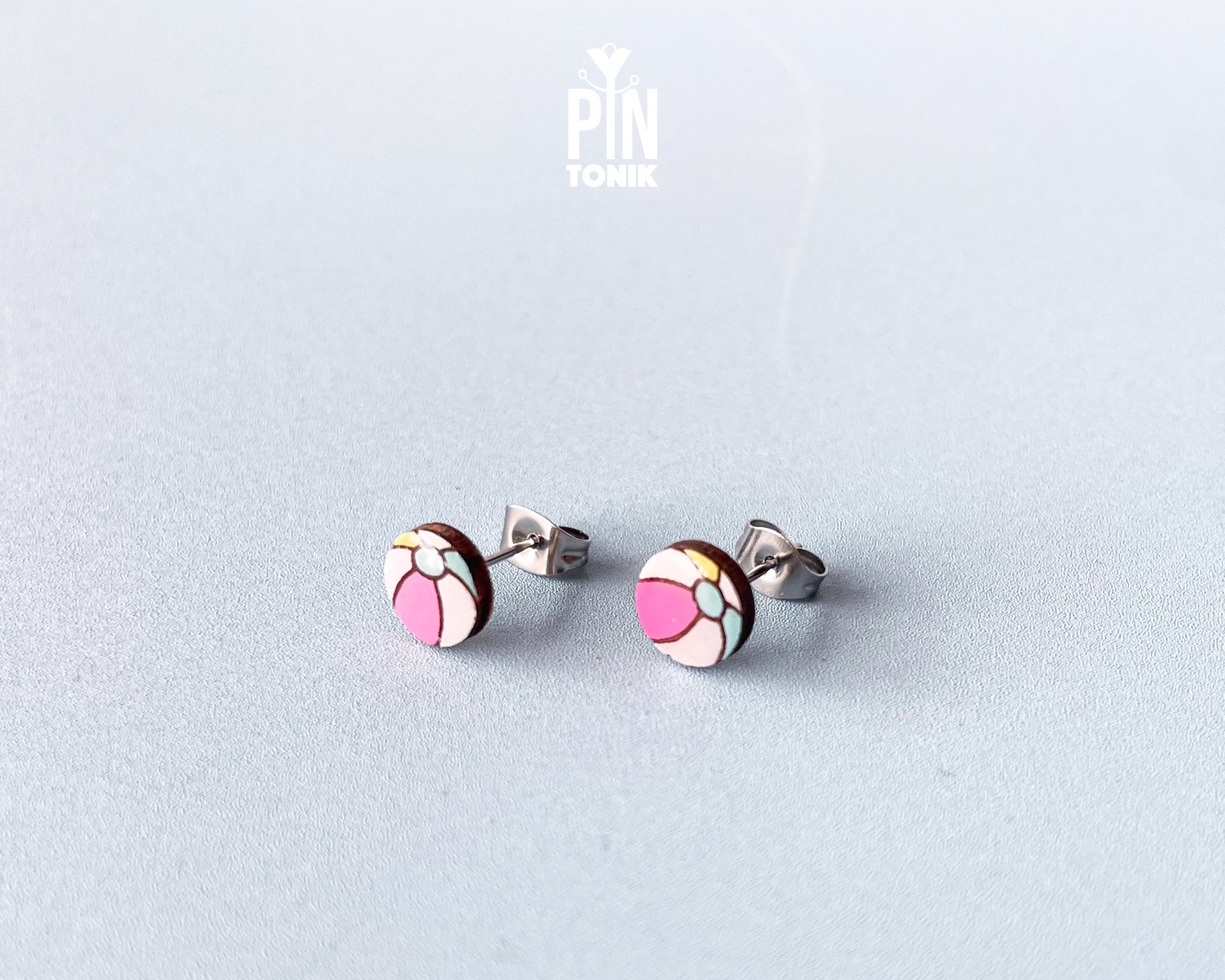 Handmade wooden beach ball stud earrings featuring a cheerful striped pattern of pink, white, and gray panels by PinTonik.