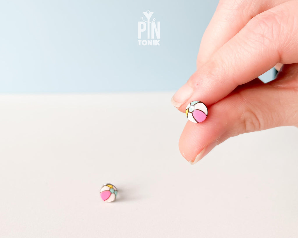 Handmade wooden beach ball stud earrings featuring a cheerful striped pattern of pink, white, and gray panels by PinTonik.