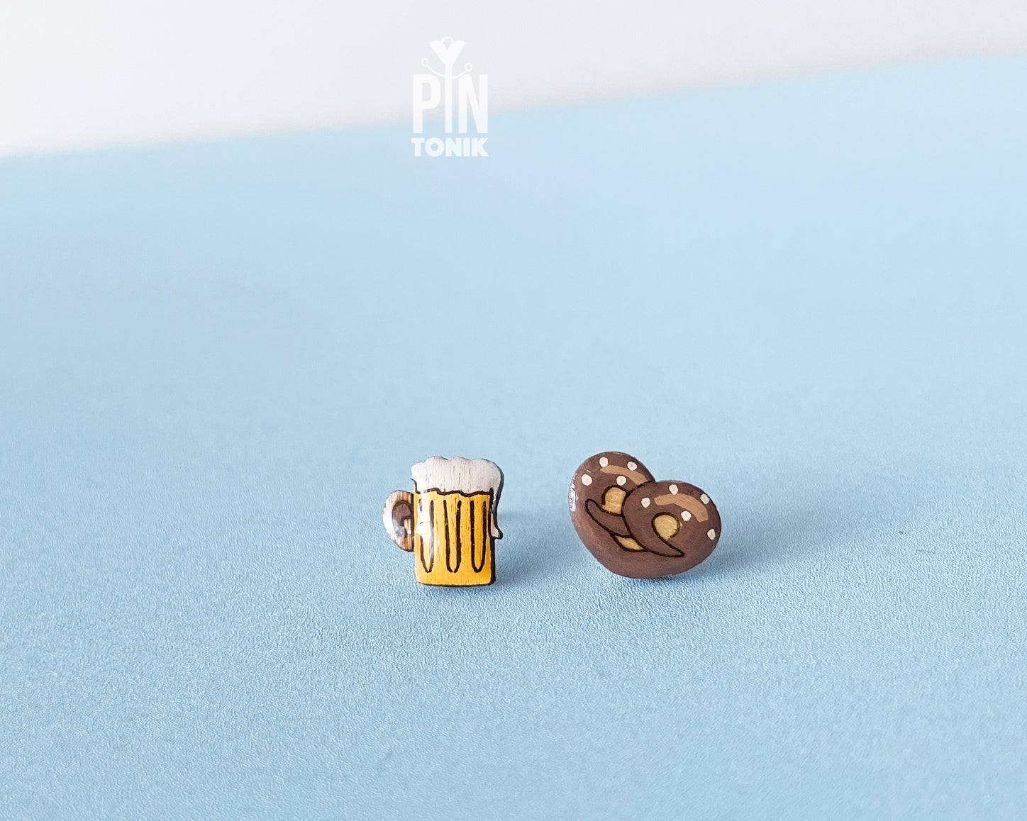 "Handmade wooden mismatched stud earrings featuring a frothy yellow beer mug on one ear and a twisted golden-brown pretzel on the other by PinTonik."