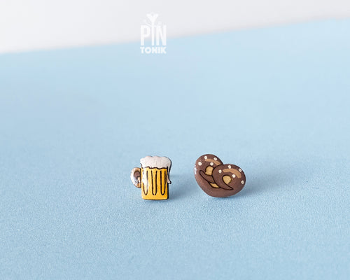 "Handmade wooden mismatched stud earrings featuring a frothy yellow beer mug on one ear and a twisted golden-brown pretzel on the other by PinTonik."