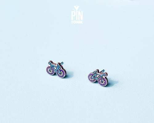 "Handmade wooden bicycle stud earrings illustrated in retro purple and blue shades by PinTonik."
