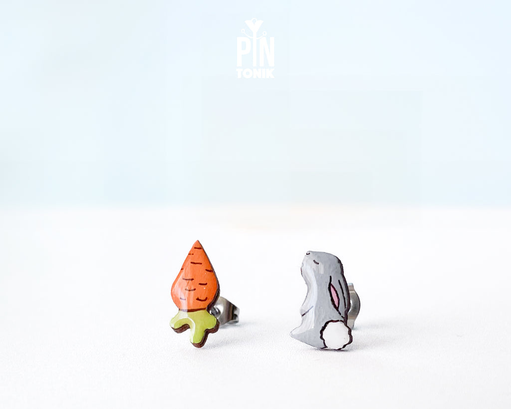 Mismatched hand-painted wooden stud earrings featuring a grey bunny and a bright orange carrot