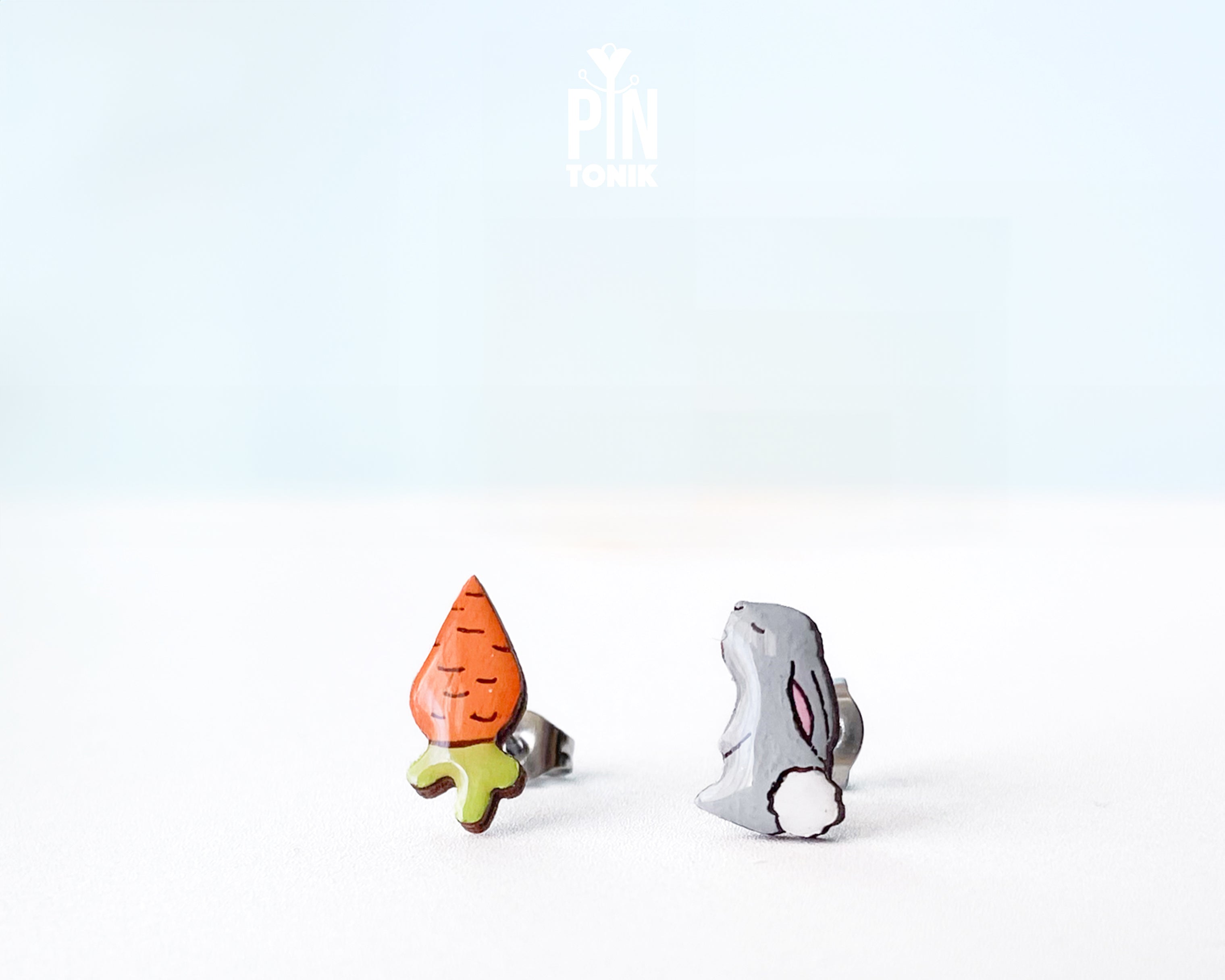 Mismatched hand-painted wooden stud earrings featuring a grey bunny and a bright orange carrot