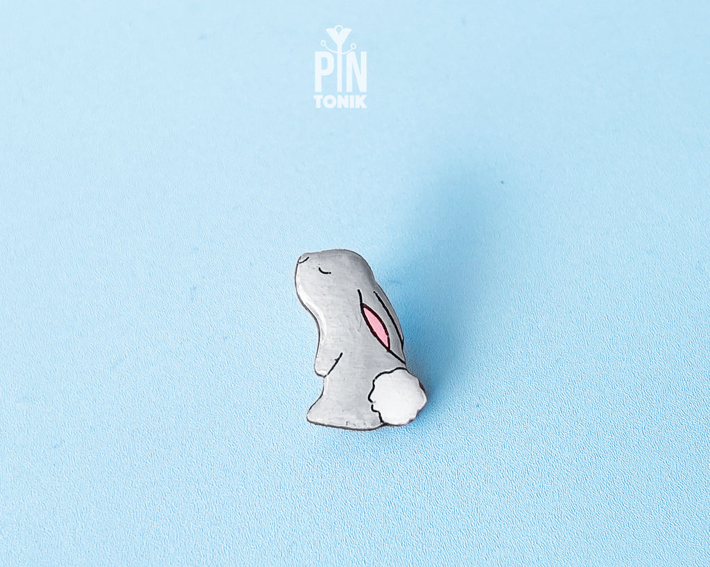 Hand-painted grey wooden bunny pin with a fluffy white tail and glossy resin finish