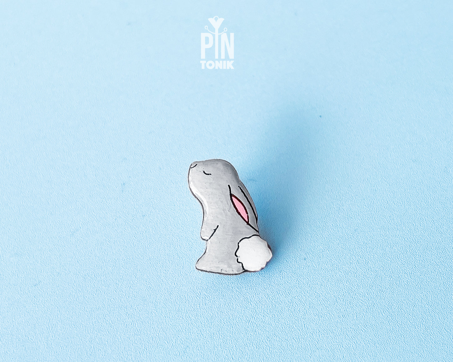 Hand-painted grey wooden bunny pin with a fluffy white tail and glossy resin finish