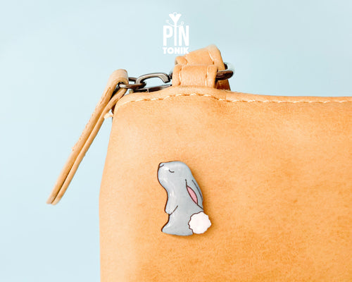 Hand-painted grey wooden bunny pin with a fluffy white tail and glossy resin finish