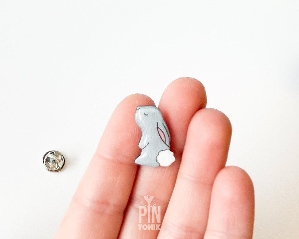 Hand-painted grey wooden bunny pin with a fluffy white tail and glossy resin finish