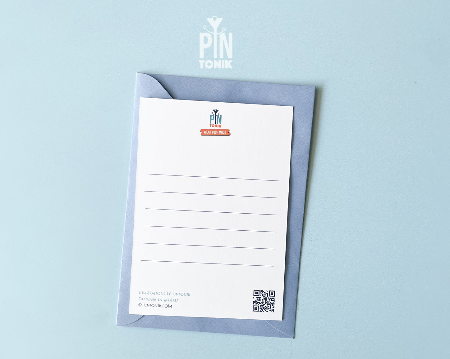 The back of a premium postcard featuring a clean, white uncoated surface with five light grey lines for a handwritten message and a QR code in the corner. An original 'PinTonik' logo with the slogan 'Wear Your Mood' is centered at the top. A luxury light blue envelope sits underneath the card against a blue background.