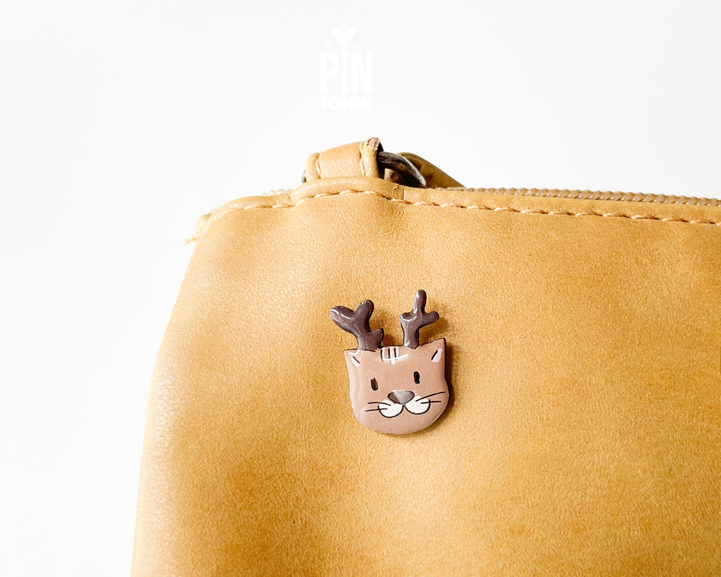 Hand-painted wooden pin featuring a cute cat wearing reindeer antlers with a glossy resin finish