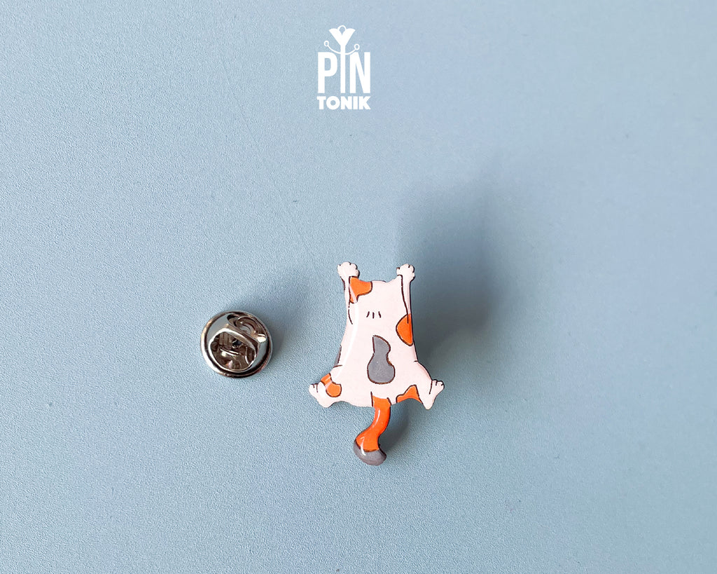 Hand-painted wooden pin of a calico cat lying flat on its belly in a sploot pose with glossy resin finish