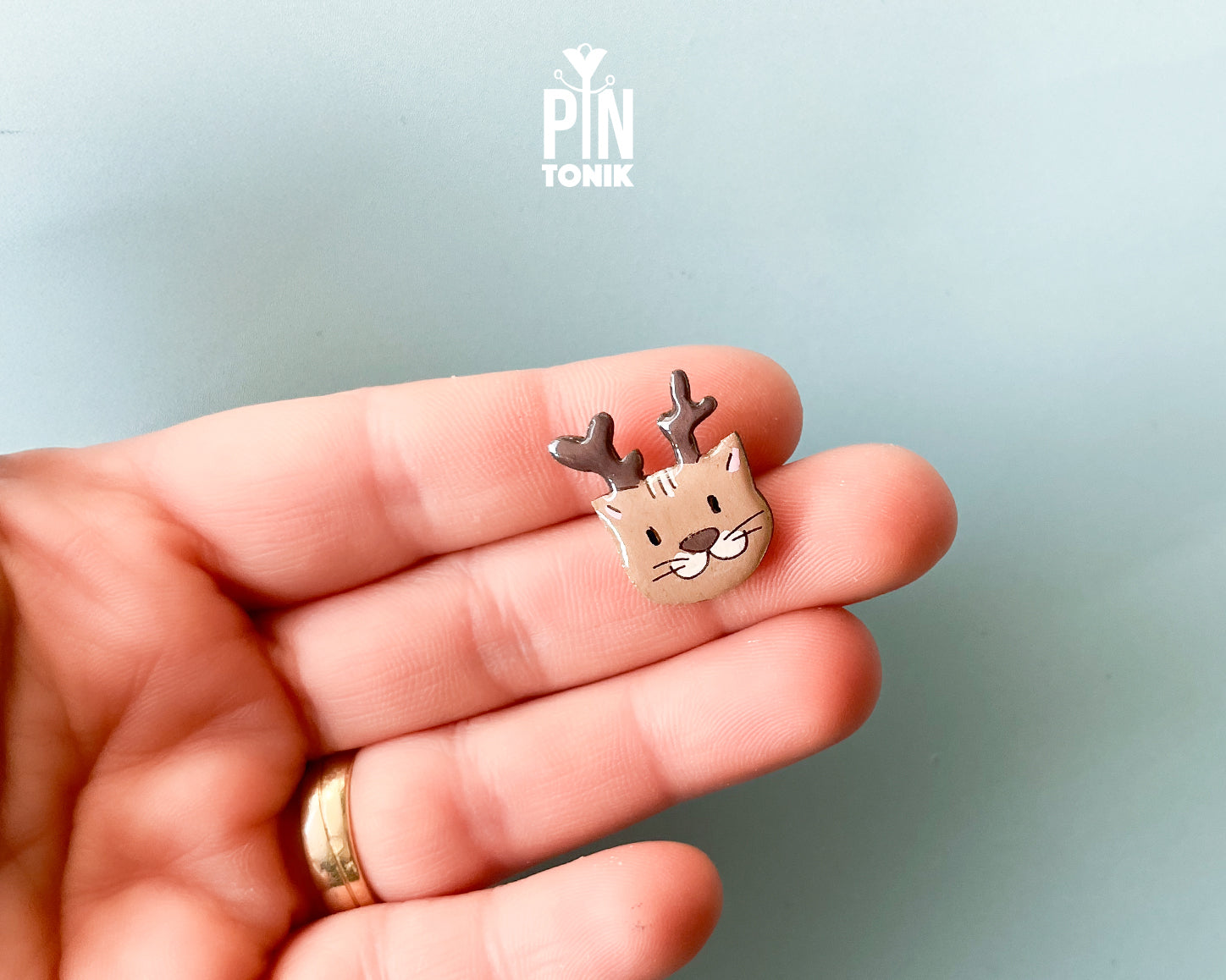 Hand-painted wooden pin featuring a cute cat wearing reindeer antlers with a glossy resin finish