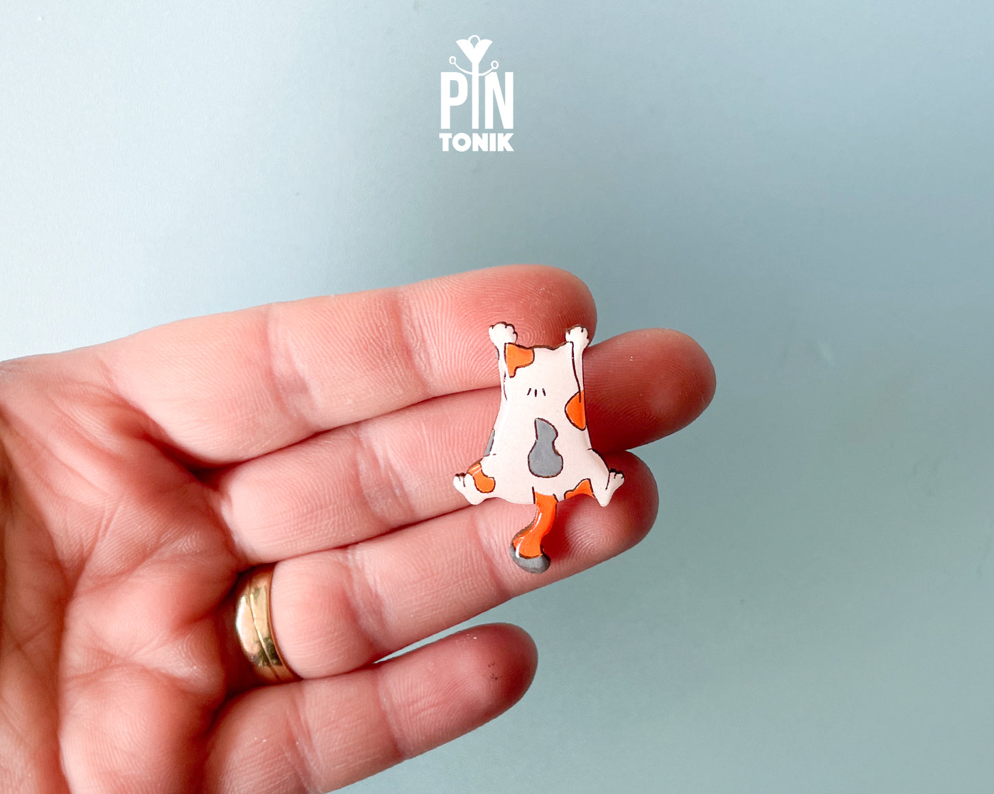 Hand-painted wooden pin of a calico cat lying flat on its belly in a sploot pose with glossy resin finish