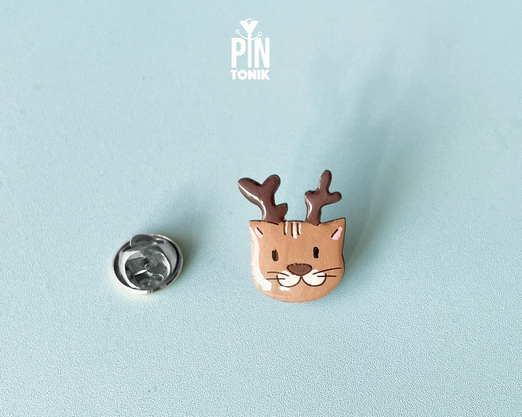 Hand-painted wooden pin featuring a cute cat wearing reindeer antlers with a glossy resin finish