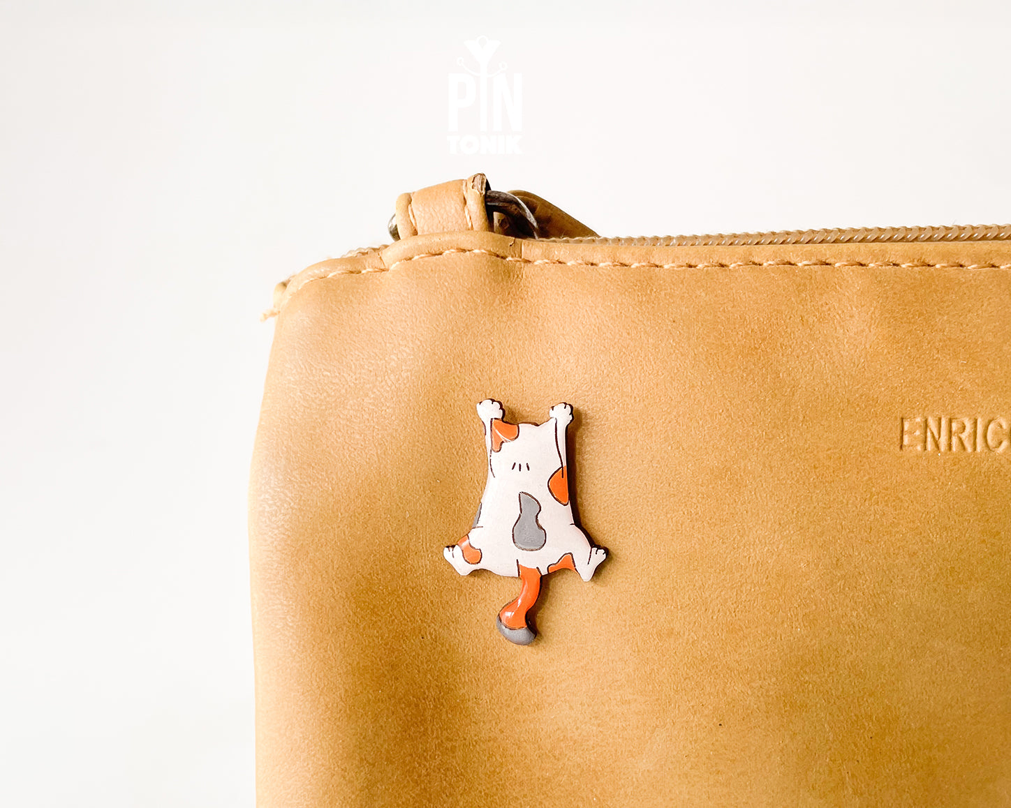 Hand-painted wooden pin of a calico cat lying flat on its belly in a sploot pose with glossy resin finish