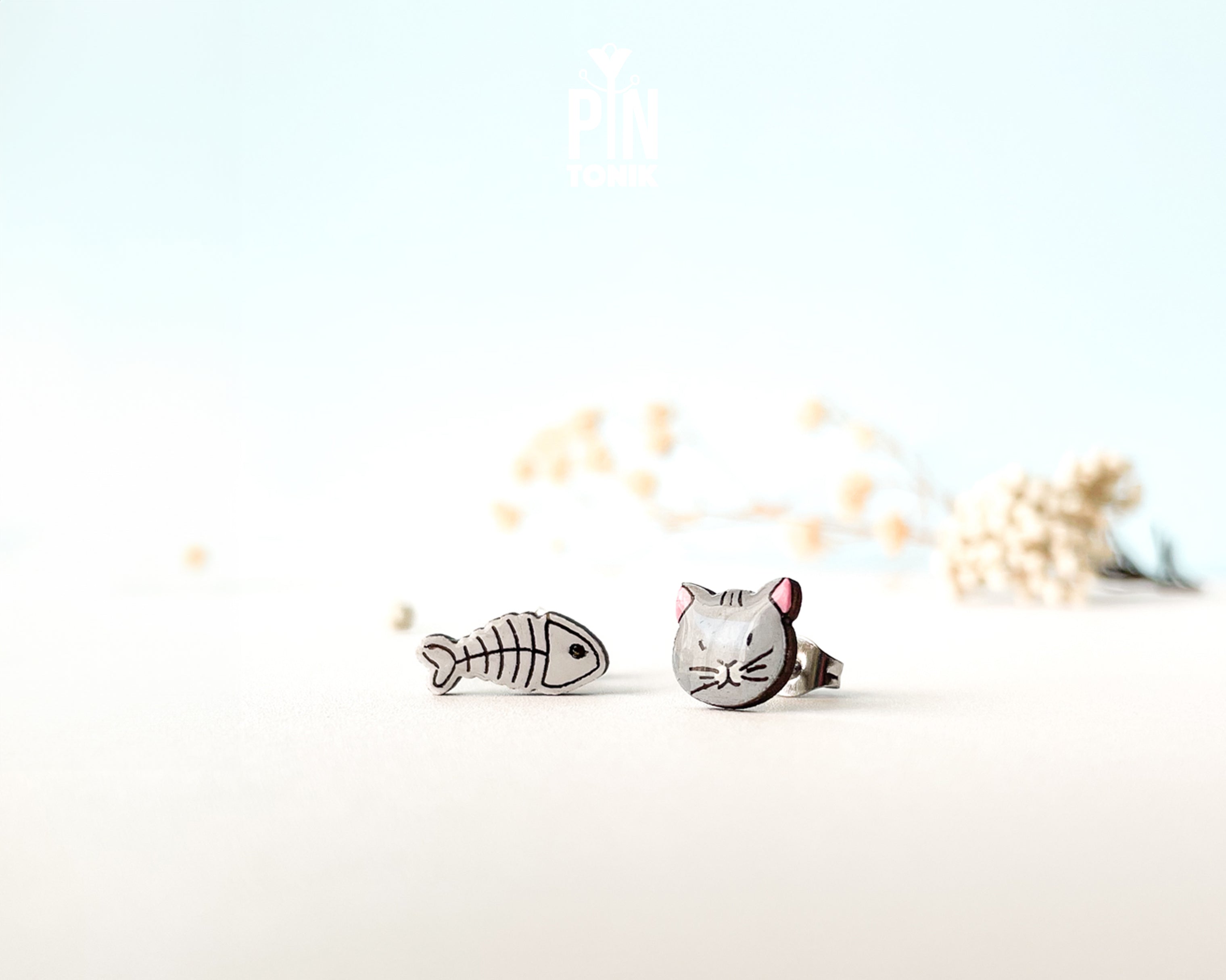 Mismatched hand-painted wooden stud earrings featuring a grey cat face and a white fishbone skeleton