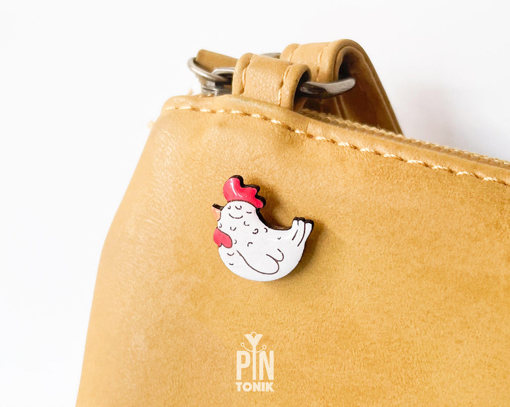 Hand-painted white wooden chicken pin with a red comb and a happy, eyes-closed expression, finished with glossy resin