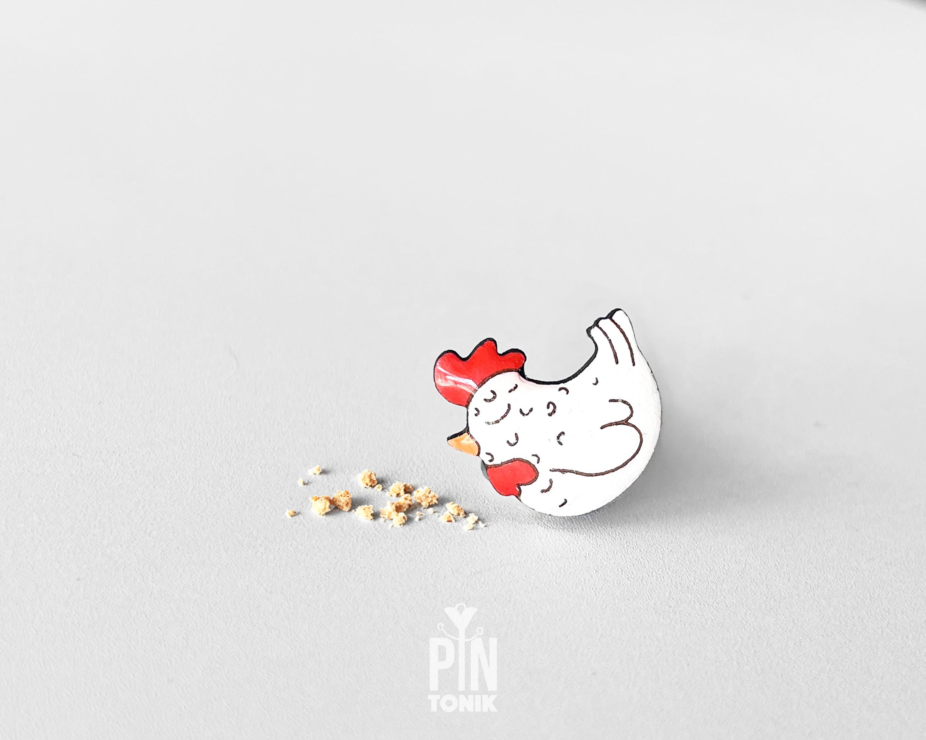 Hand-painted white wooden chicken pin with a red comb and a happy, eyes-closed expression, finished with glossy resin