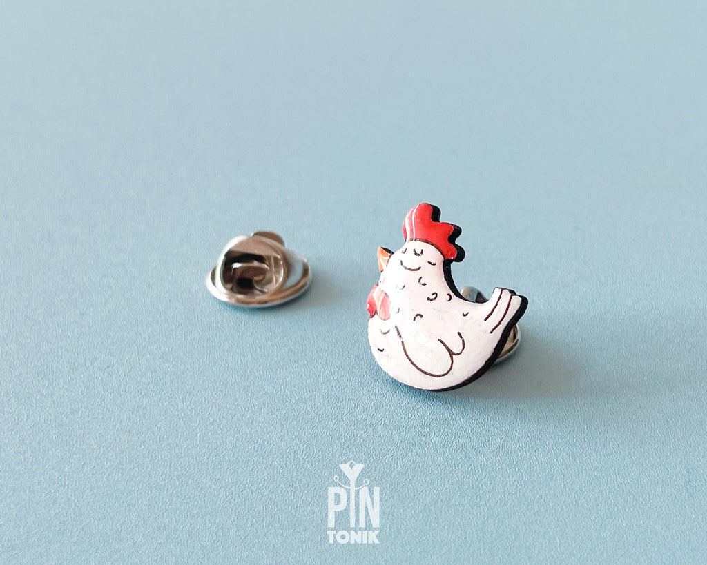Hand-painted white wooden chicken pin with a red comb and a happy, eyes-closed expression, finished with glossy resin