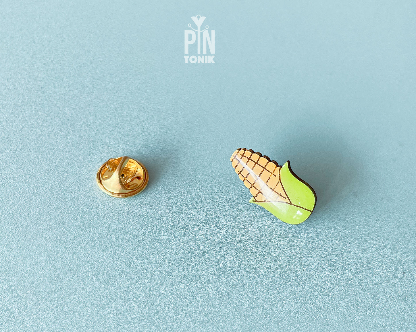 Hand-painted wooden pin of an ear of corn with bright green husks and a high-gloss resin finish