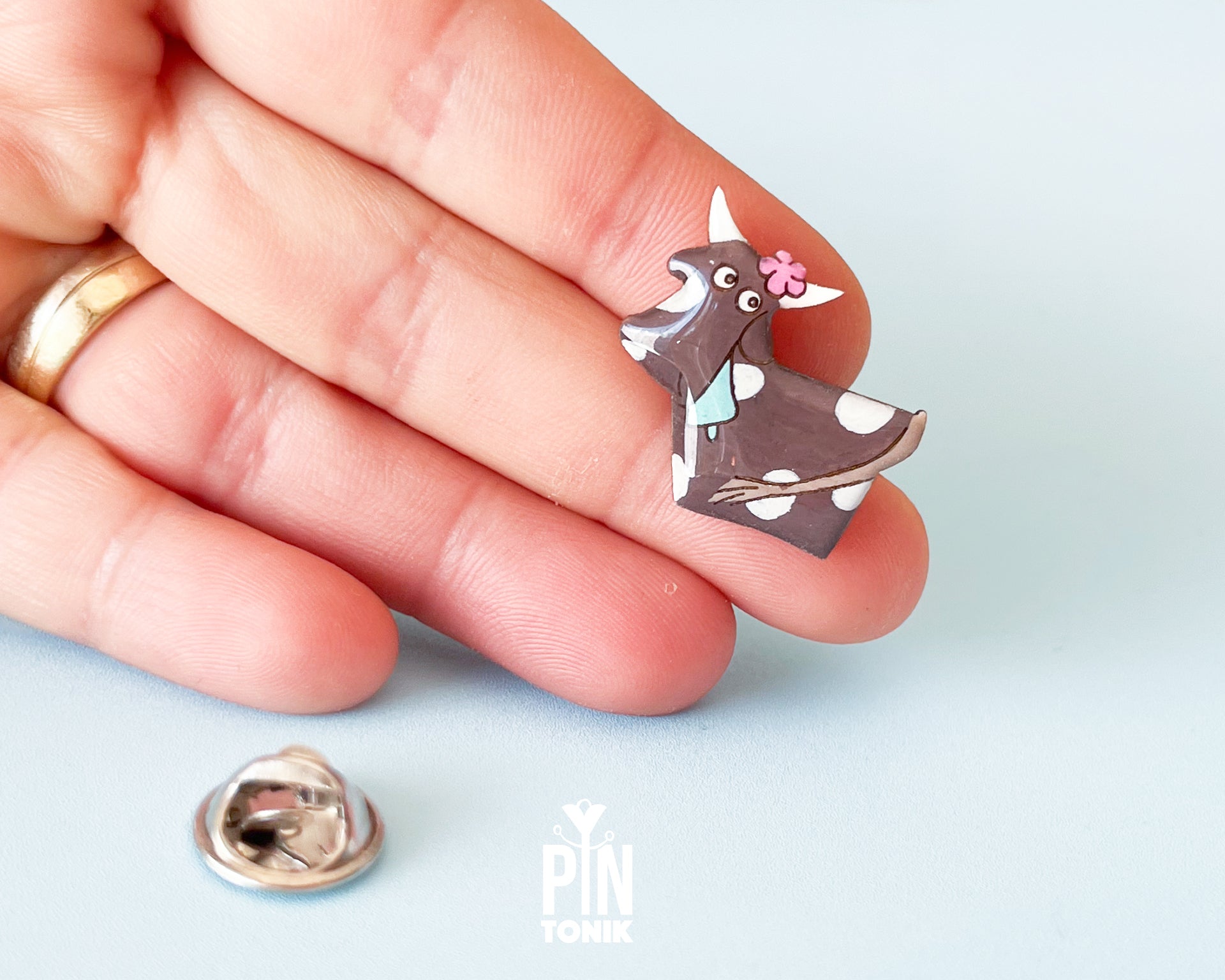 Hand-painted brown and white wooden cow pin with a pink flower and a glossy resin finish