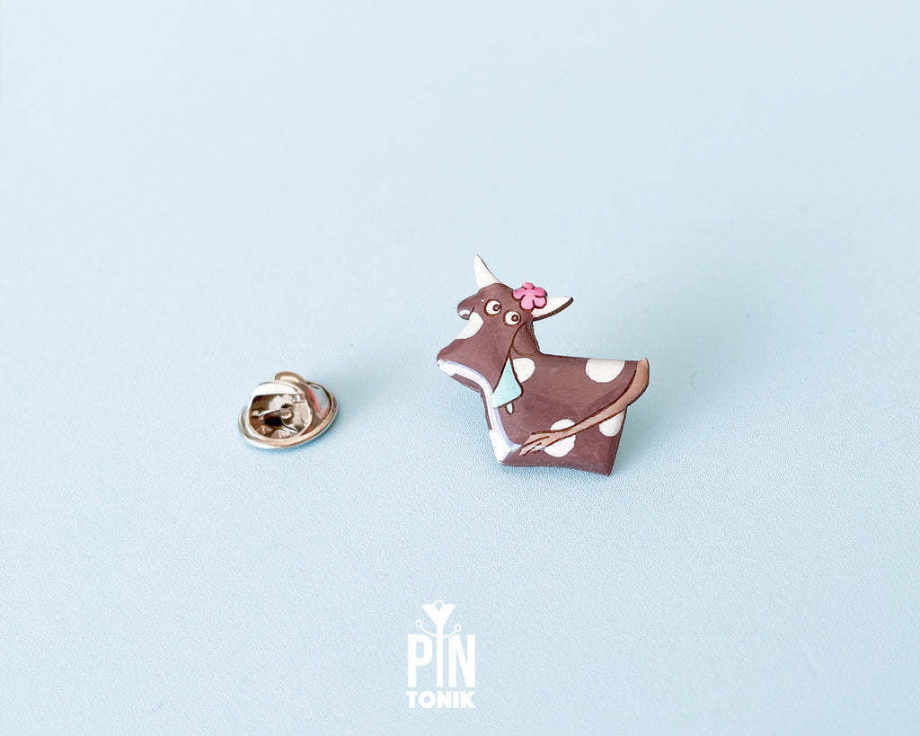 Hand-painted brown and white wooden cow pin with a pink flower and a glossy resin finish