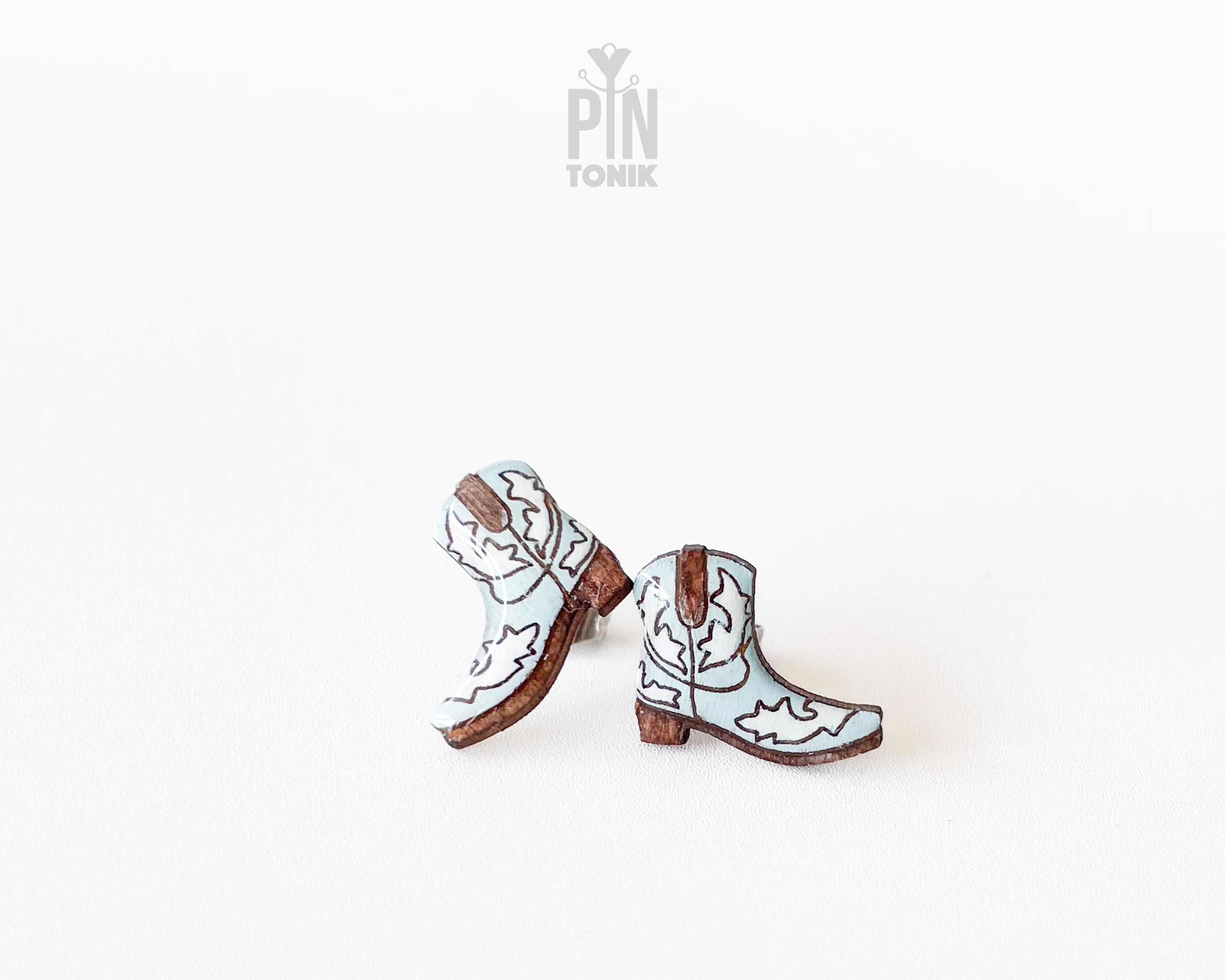 Handmade wooden cowboy boot stud earrings with detailed white and brown Western leather style illustrations by PinTonik.